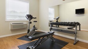 Ein Fitnessstudio mit Trainingsgeräten, einer Hantelbank, einem Hantelständer und einem an der Wand montierten Fernseher.