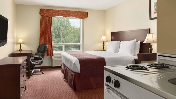 Habitación de hotel con cama, escritorio, silla, televisión, ventana con cortinas y estufa.