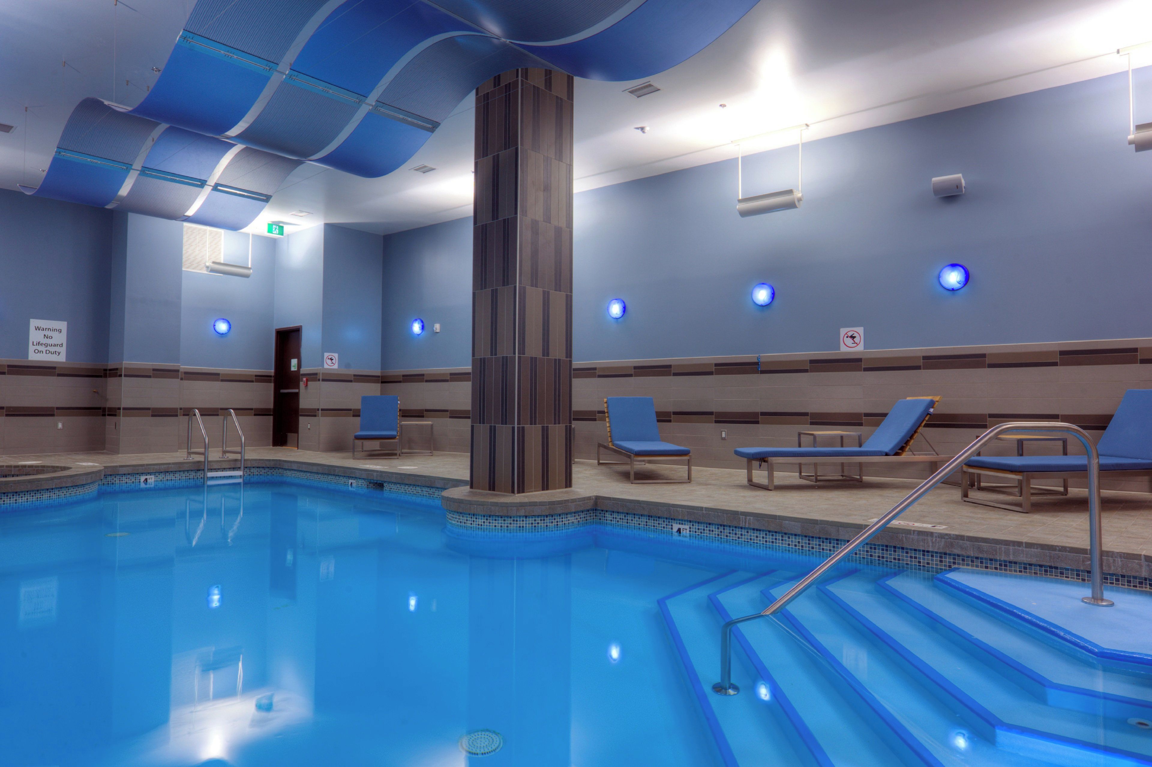Piscina com degraus de acesso, rodeada por espreguiçadeiras e um design de teto moderno.