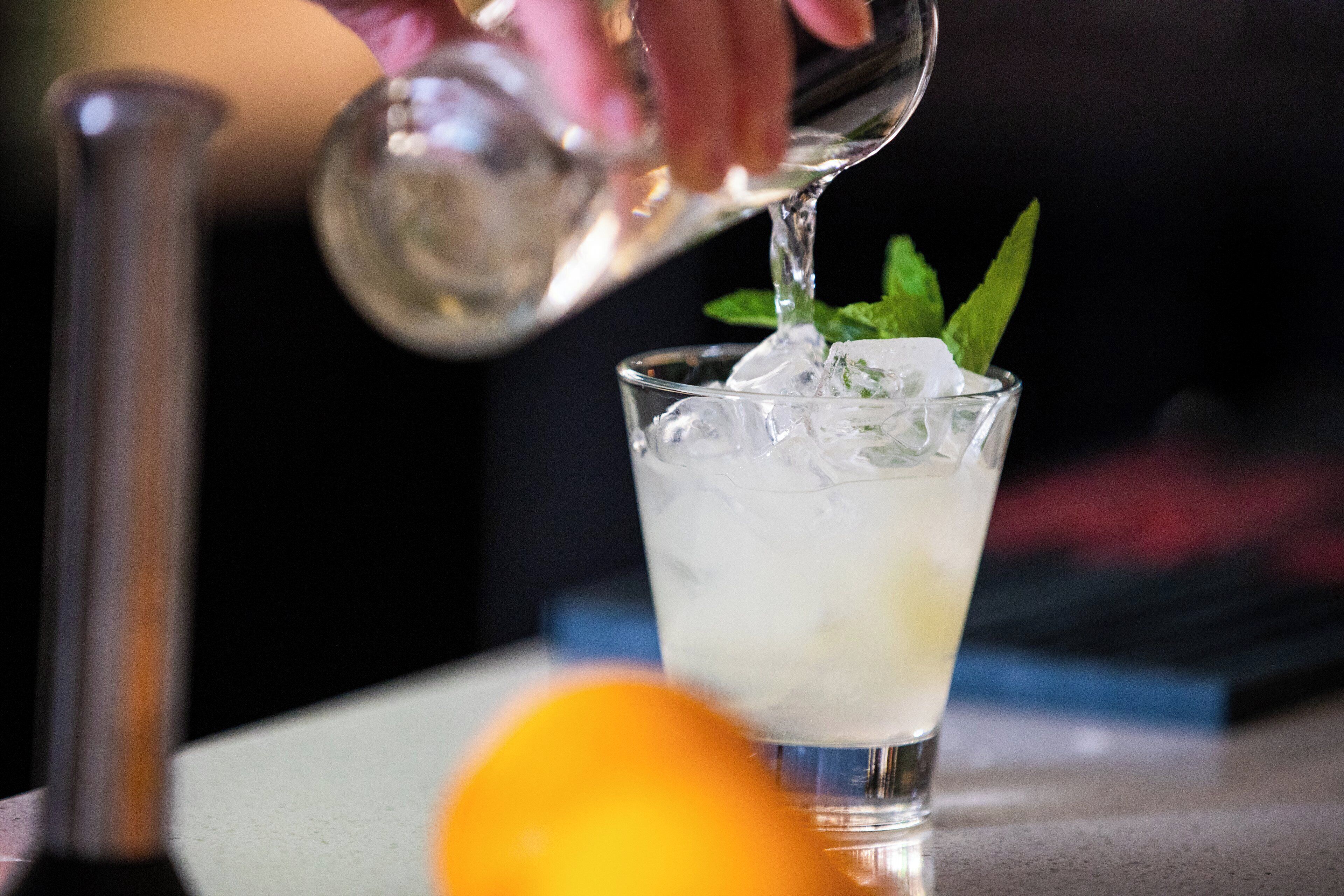 A cocktail being poured into a glass with ice and mint leaves.