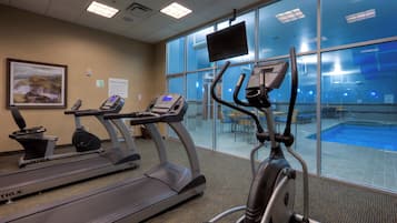 Un gimnasio con cintas de correr, una máquina elíptica y vistas a la piscina.