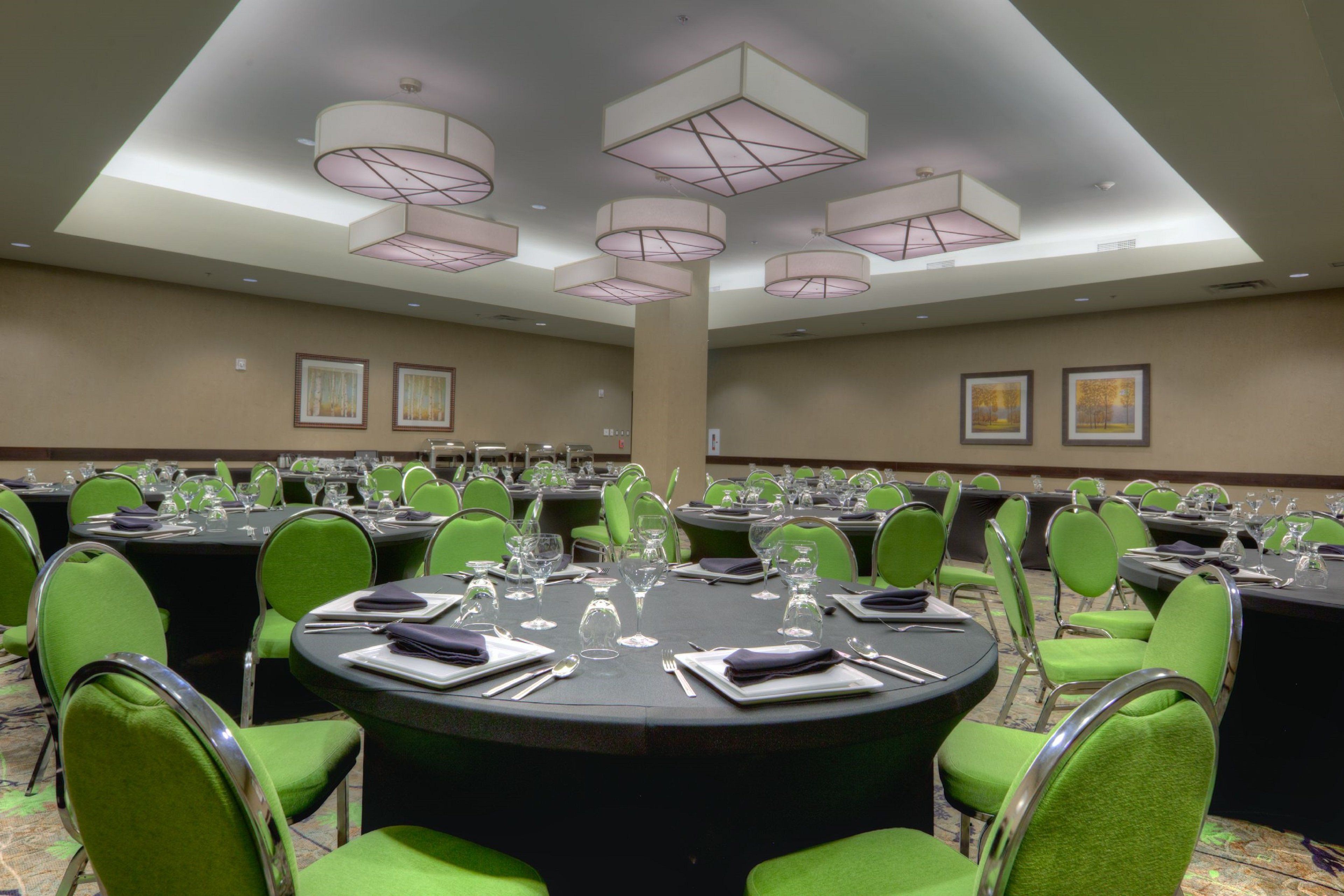 Un salón de conferencias con mesas redondas, sillas verdes e iluminación suspendida.