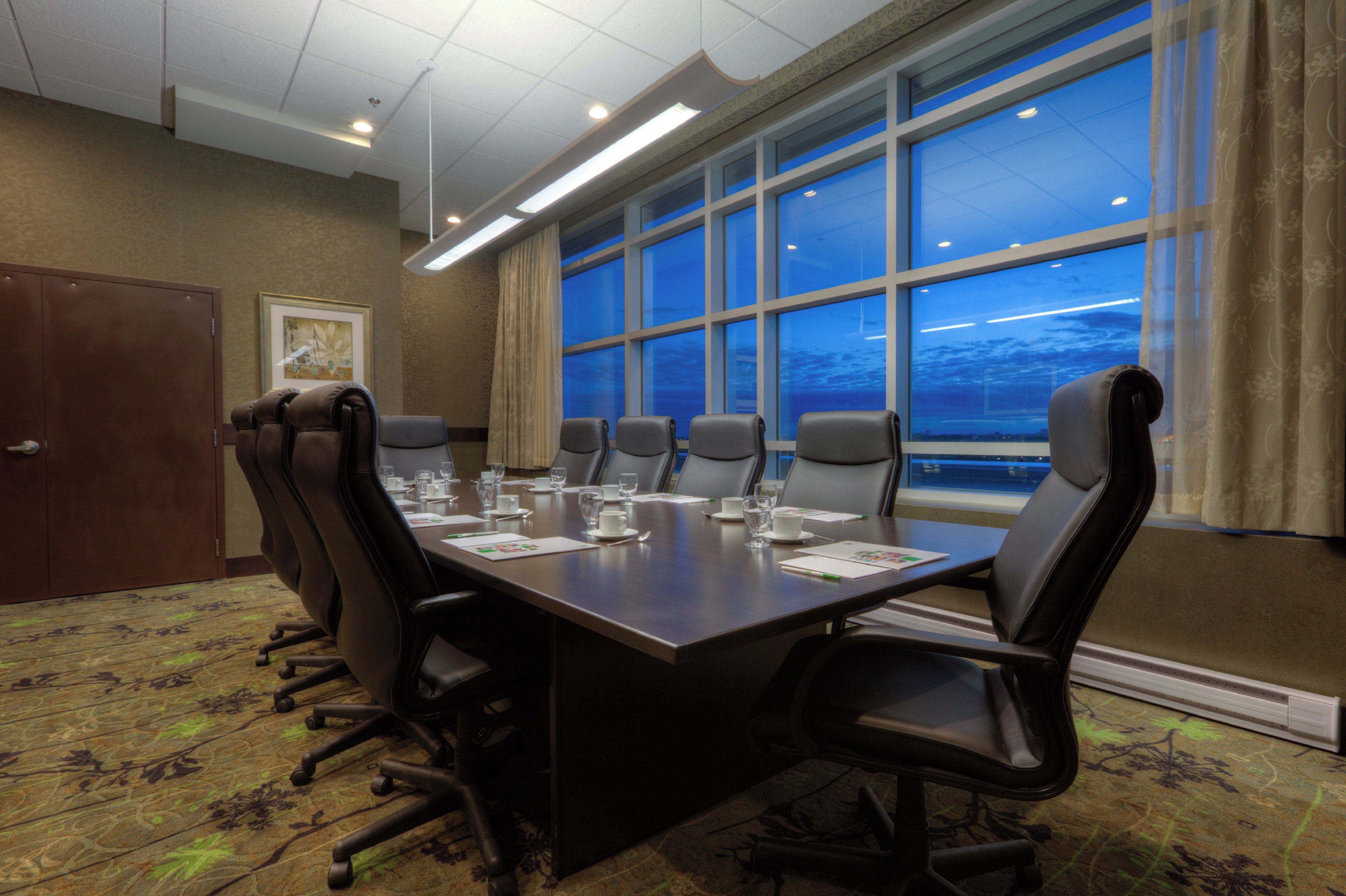 A conference room with a long table, multiple chairs, and a view of the sky through large windows.