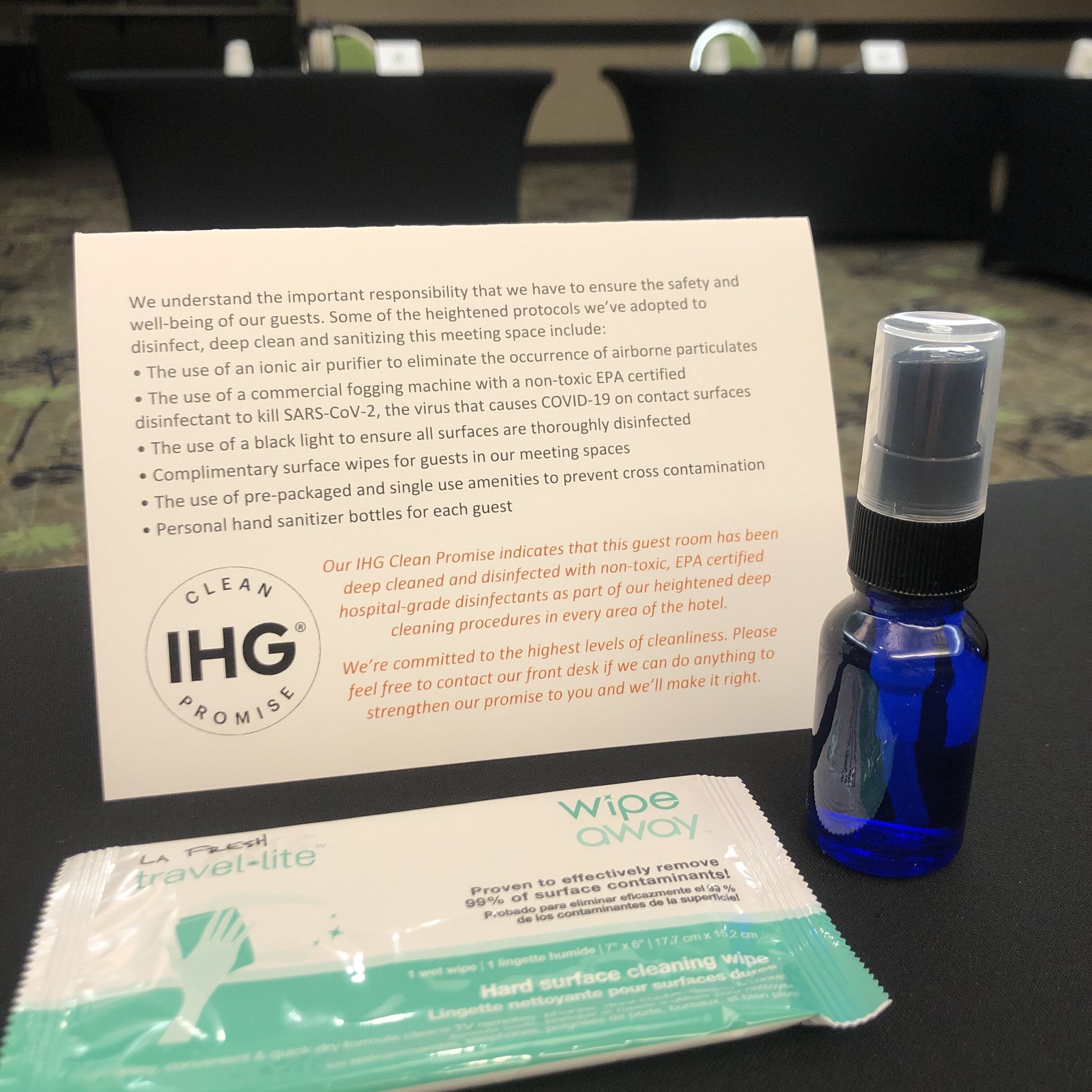 A hotel room with a sign detailing cleaning procedures, a blue spray bottle, and a travel-size hand sanitizer packet.