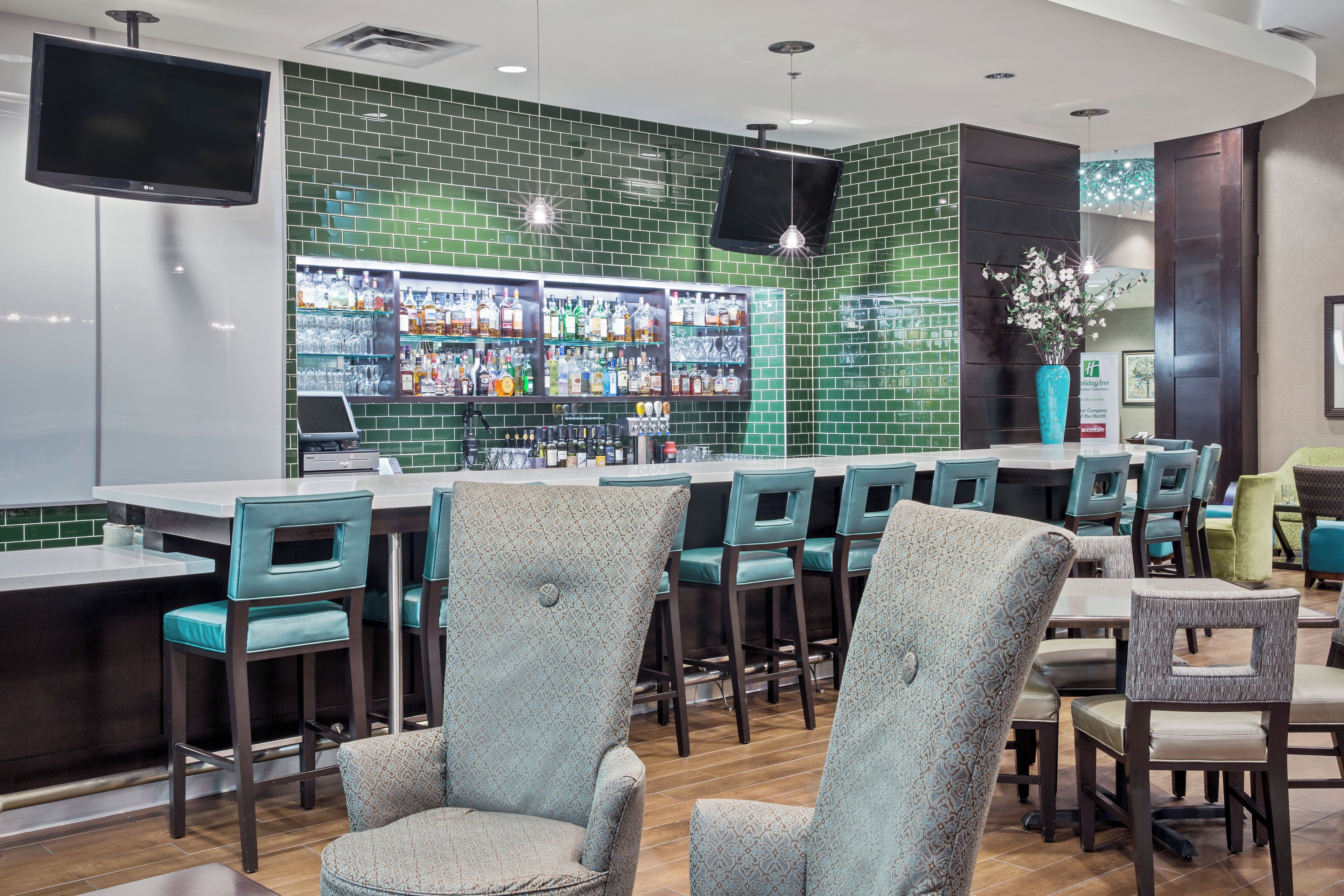 A bar area with green tiled walls, a flat-screen TV, and a variety of liquor bottles.