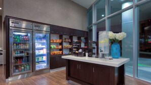 A commercial kitchen with two refrigerators stocked with beverages, a coffee machine, and a vase with flowers on the counter. - Holiday Inn Hotel & Suites Saskatoon Downtown by IHG (Saskatoon)
