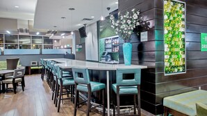 A modern bar area with a long counter, bar stools, and a decorative wall with a green mosaic. - Holiday Inn Hotel & Suites Saskatoon Downtown by IHG (Saskatoon)