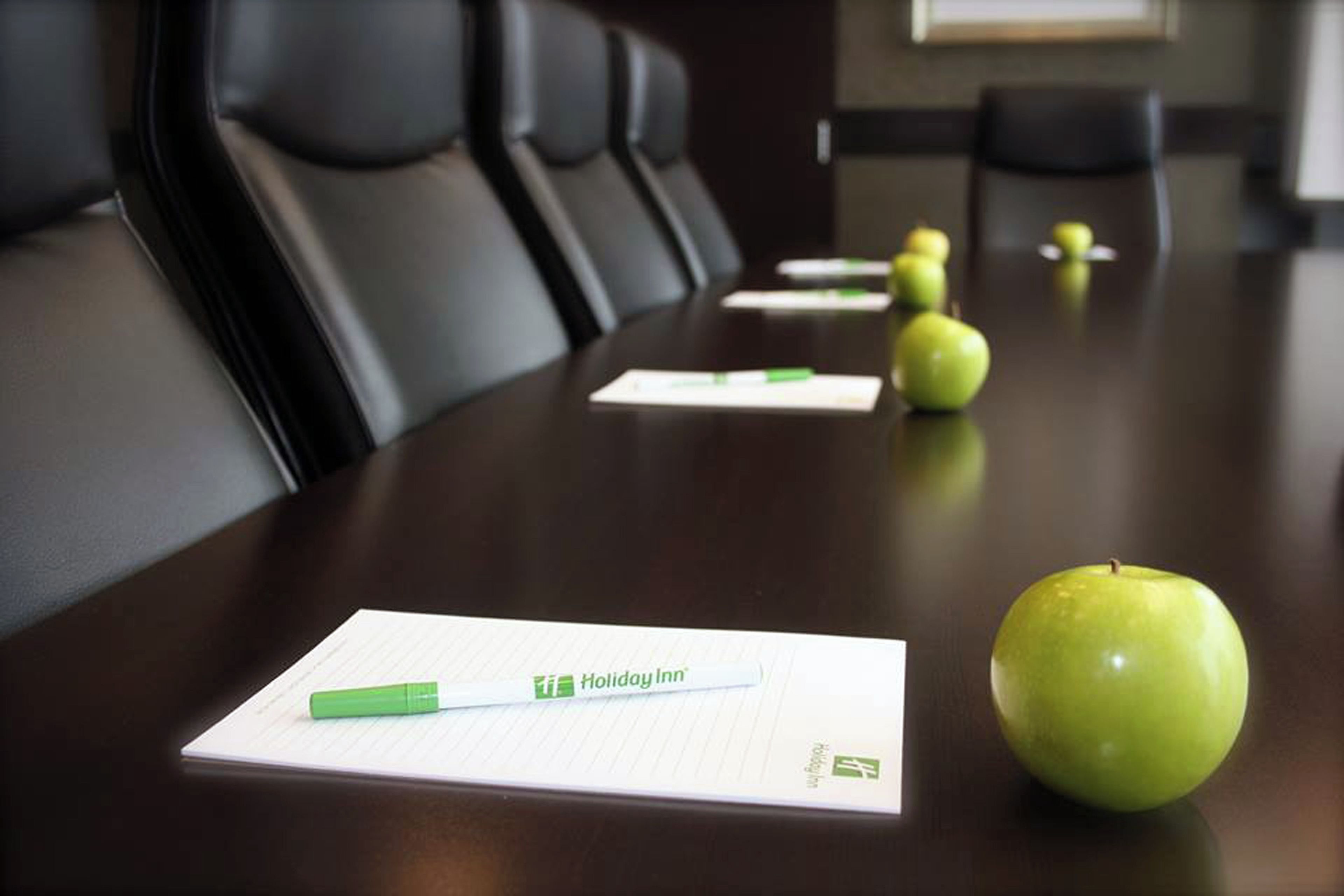 Una mesa de conferencias con papeles, un bolígrafo y una manzana verde encima.