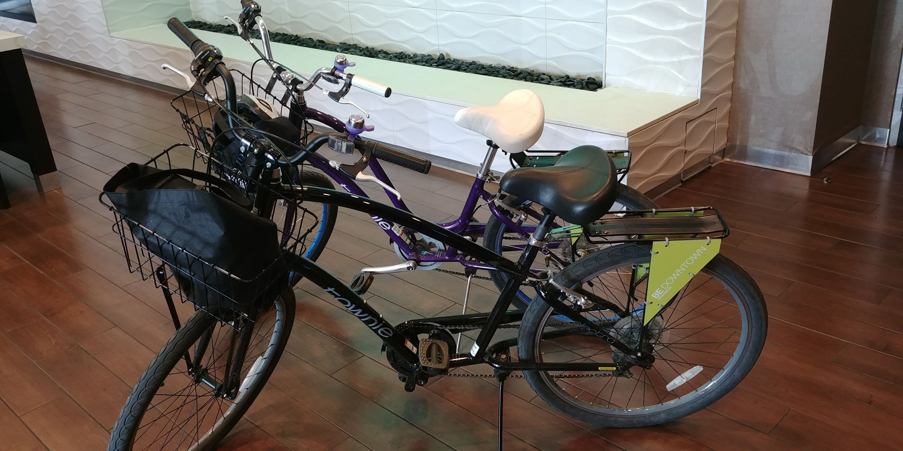 A bicycle with a basket and a seat, parked indoors with a tiled floor and a decorative wall in the background.