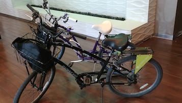 A bicycle with a basket and a seat, parked indoors with a tiled floor and a decorative wall in the background.