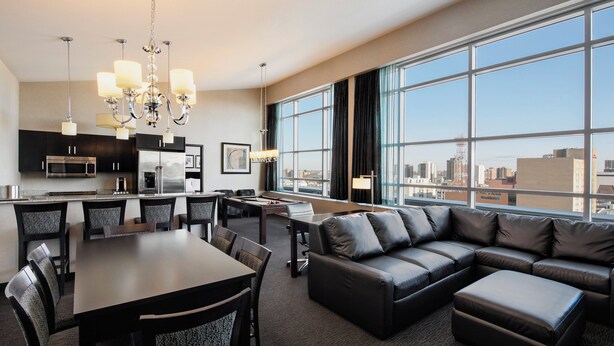 A modern hotel room with a dining area, a pool table, a leather sofa, and a city view. - Holiday Inn Hotel & Suites Saskatoon Downtown by IHG (Saskatoon)