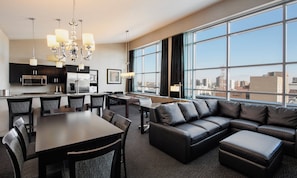 A modern hotel room with a dining area, a pool table, a leather sofa, and a city view.
