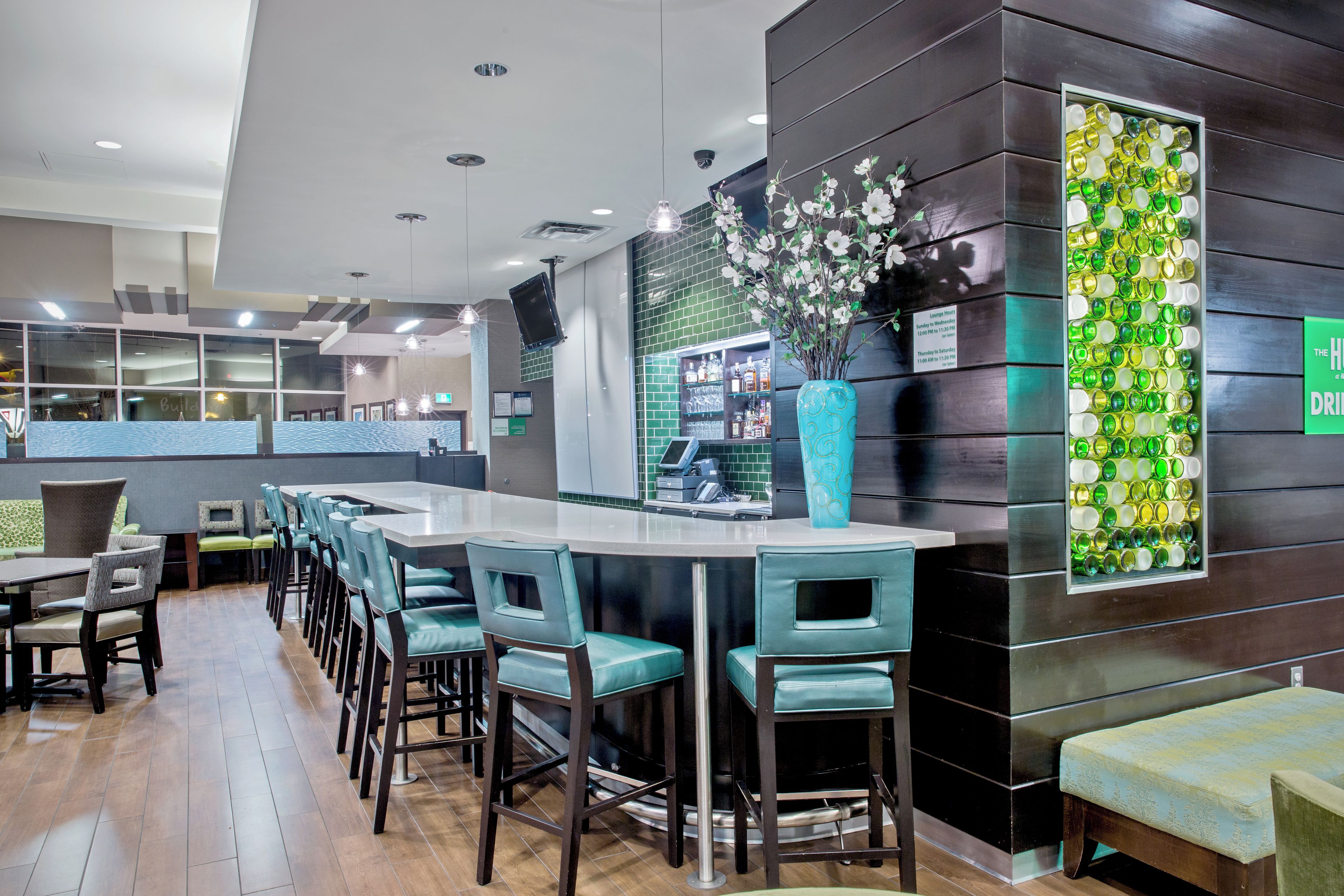 Zona de bar con mostrador, taburetes, un jarrón decorativo y una pared con mosaico verde.