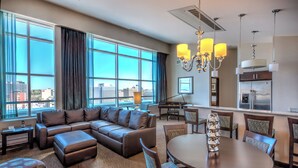 A modern hotel room with a large sectional sofa, a dining table with chairs, a piano, and a kitchen area. - Holiday Inn Hotel & Suites Saskatoon Downtown by IHG (Saskatoon)