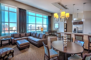 A modern hotel room with a large sectional sofa, a dining table with chairs, a piano, and a kitchen area. - Holiday Inn Hotel & Suites Saskatoon Downtown by IHG (Saskatoon)