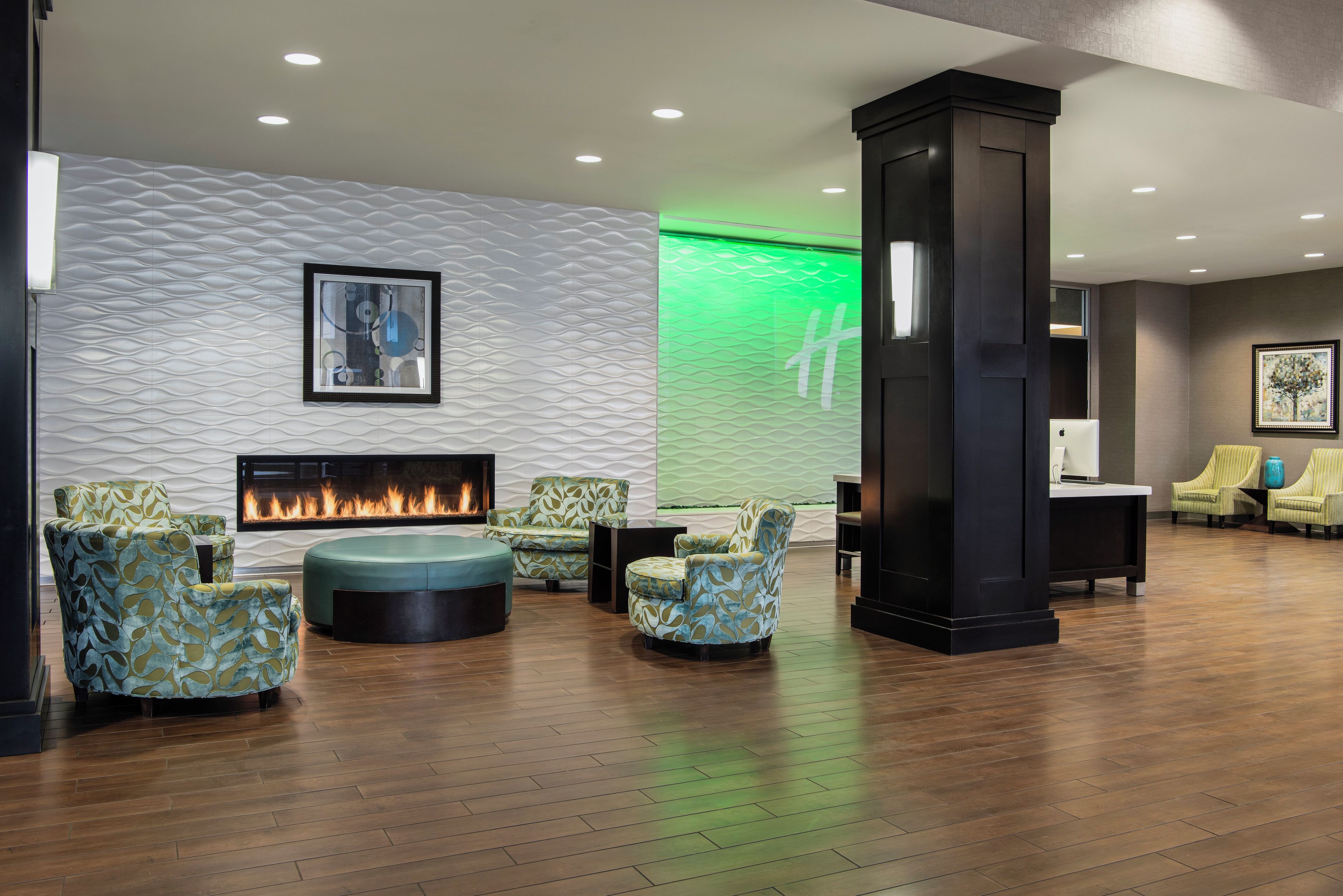 A modern lounge area with a fireplace, seating, and a green-lit wall.