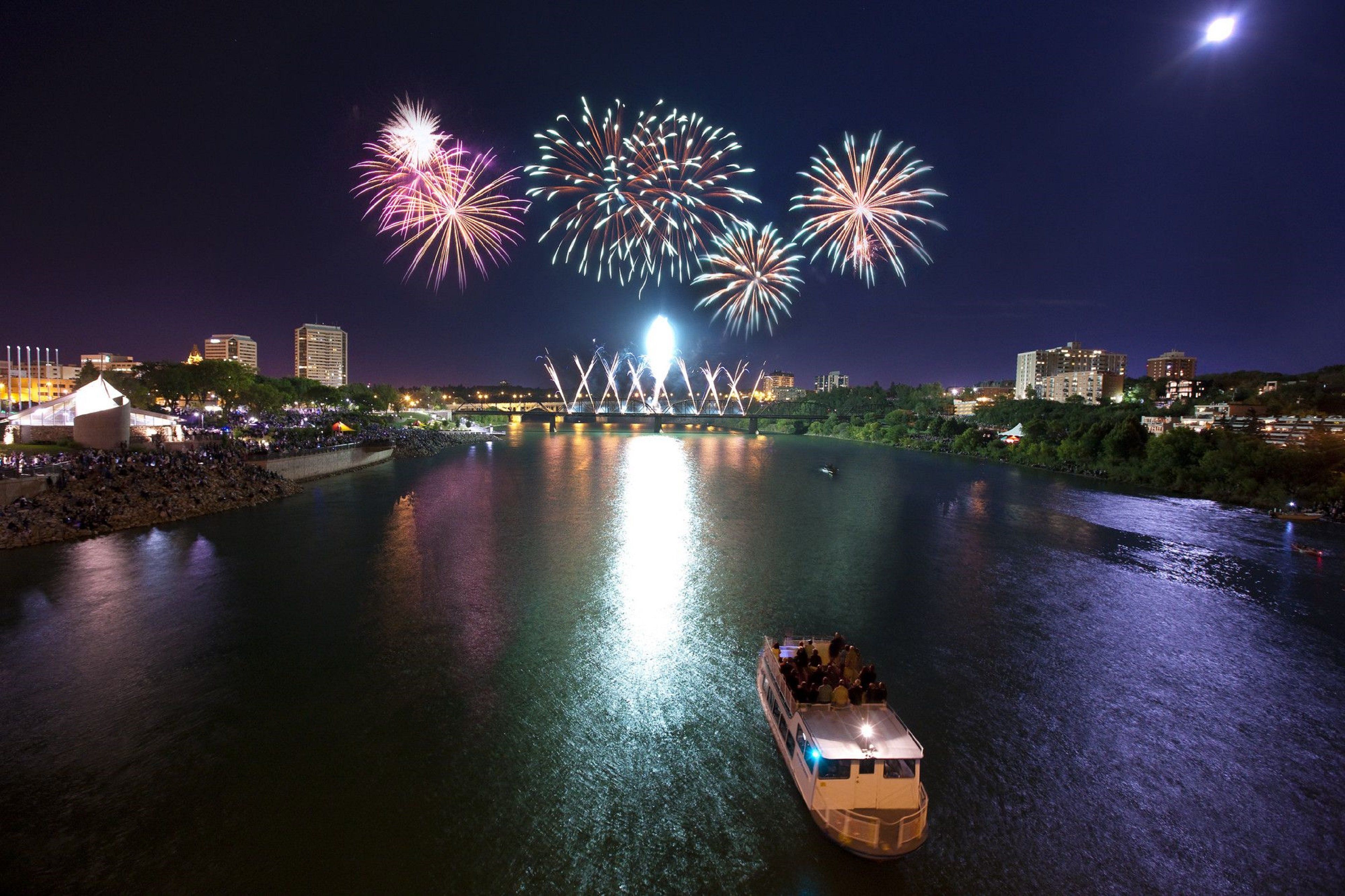 A river with a boat and fireworks in the background.