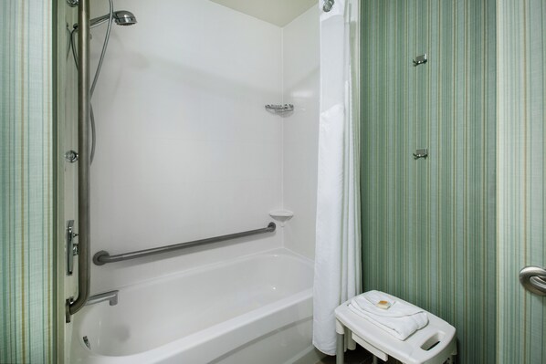 A bathroom with a bathtub, a shower, a toilet, and a handrail.