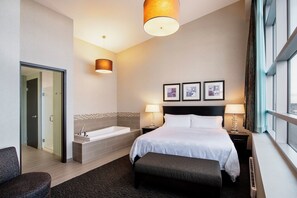 A hotel room with a large bed, a sitting area, a bathtub, and a window with a view. - Holiday Inn Hotel & Suites Saskatoon Downtown by IHG (Saskatoon)