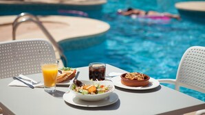 A dining table with breakfast items and a glass of orange juice by a poolside.