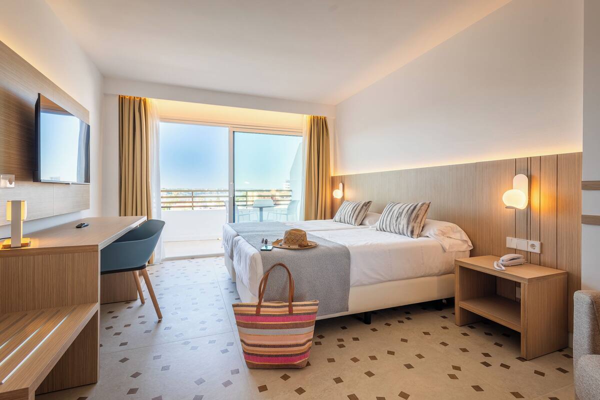 Une chambre d’hôtel avec un lit, un bureau, une chaise et une grande fenêtre.