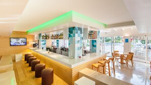 A modern bar area with a long counter, stools, and a television screen.
