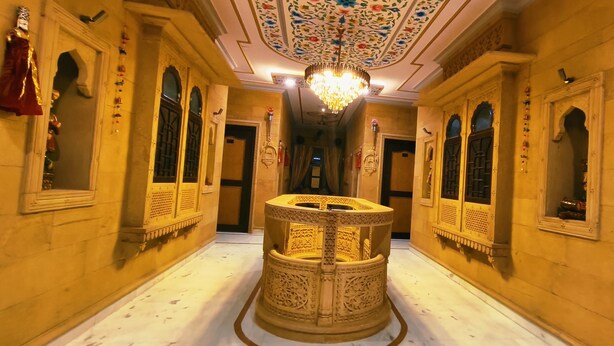 A corridor with ornate walls, a central decorative column, and a chandelier. - Hotel Moonlight (Jaisalmer)