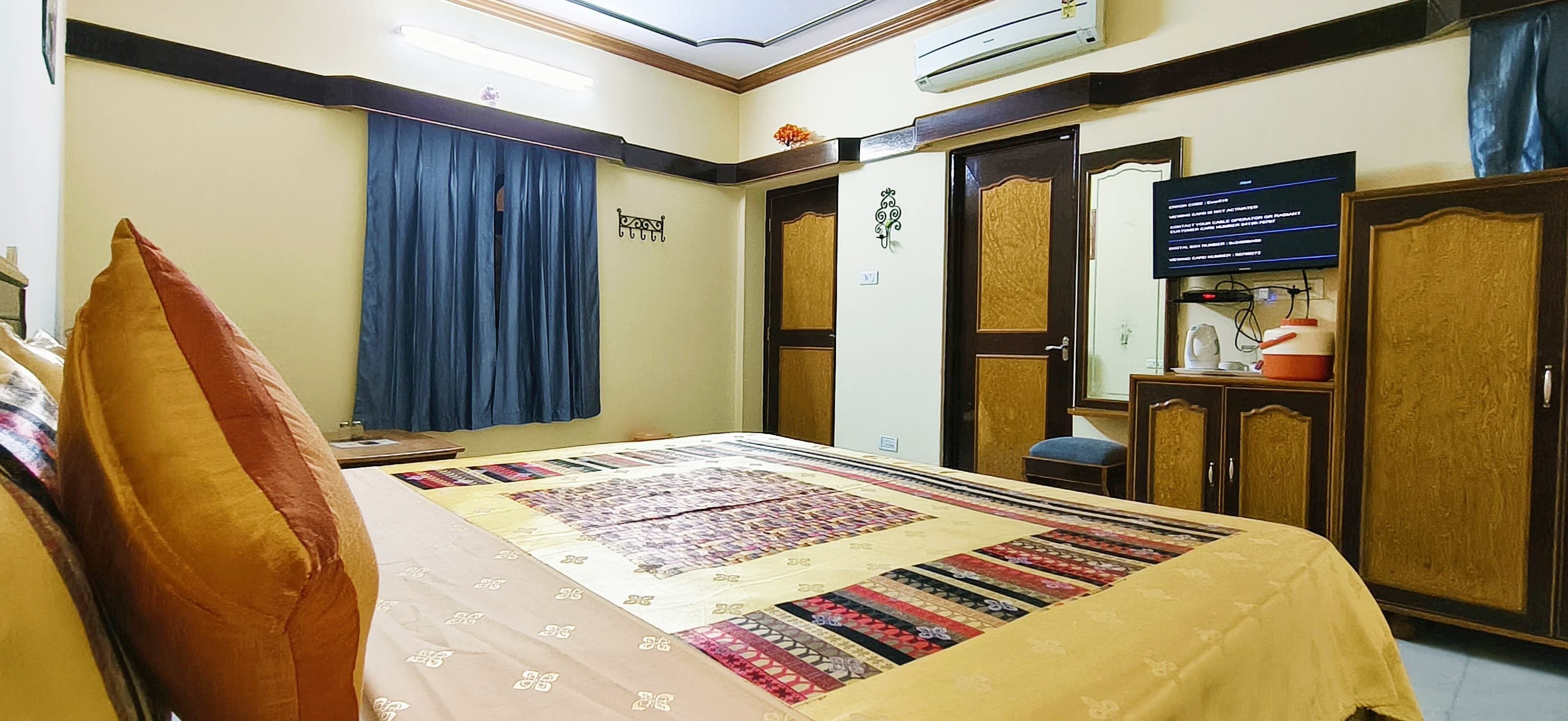 A hotel room with a bed, a desk, a chair, a wardrobe, and an air conditioning unit.