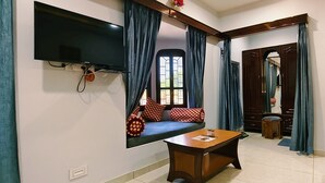 A room with a TV mounted on the wall, a sofa with patterned cushions, a small table, and a bed with a yellow bedspread. - Hotel Moonlight (Jaisalmer)