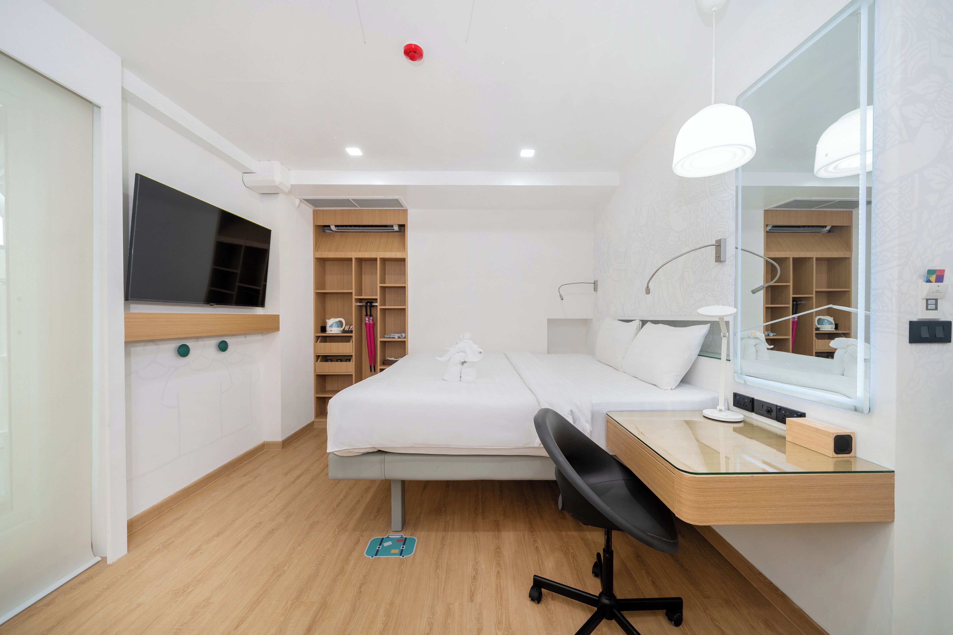 Una habitación de hotel moderna con cama, escritorio, silla, televisor y un espejo grande.