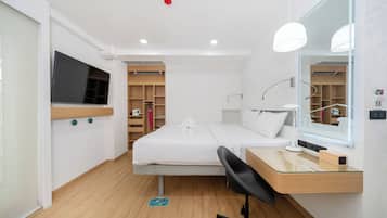 Una habitación de hotel moderna con cama, escritorio, silla, televisor y un espejo grande.