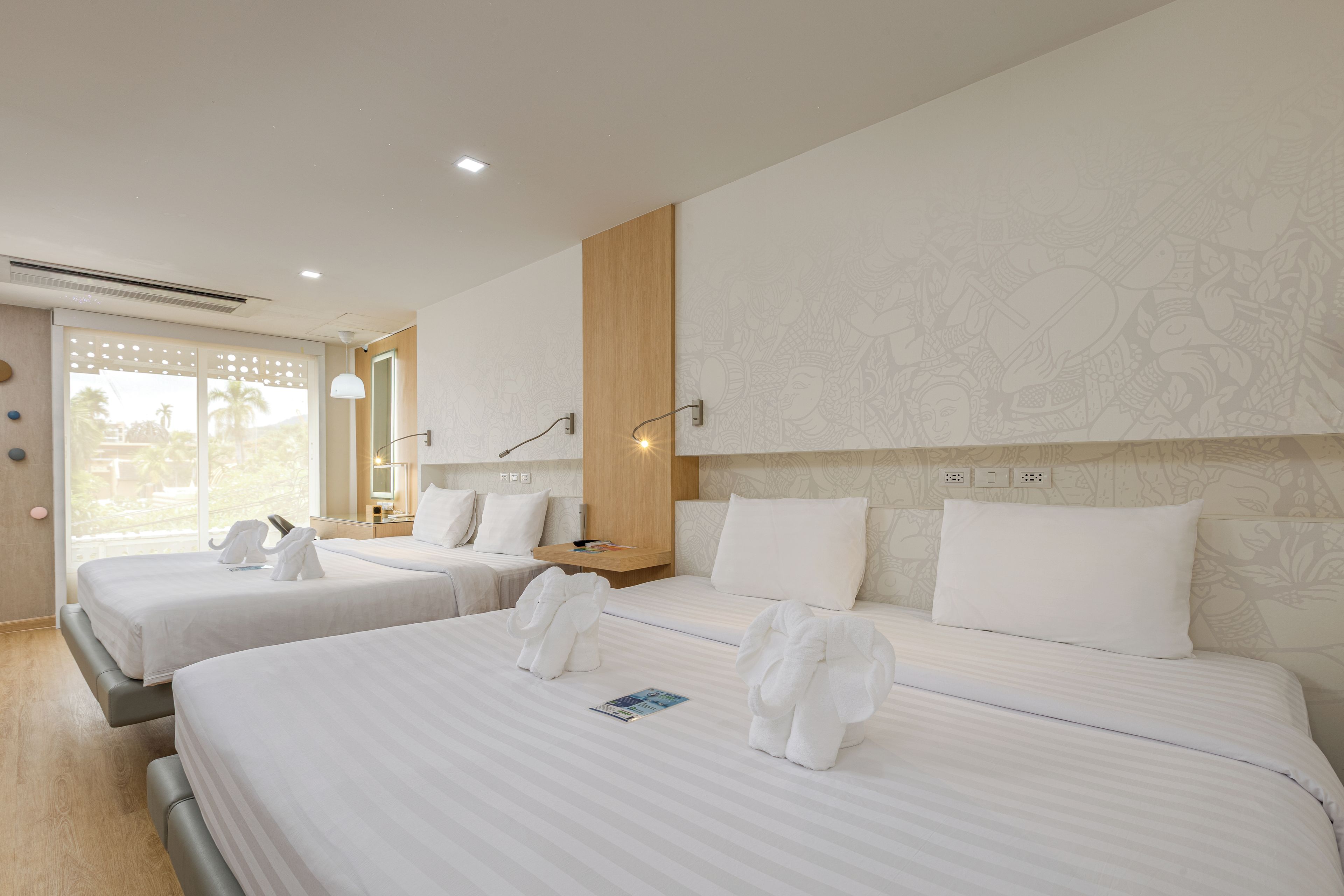 A hotel room with two beds, a wooden headboard, a wall with a decorative pattern, and a window with a view of palm trees.