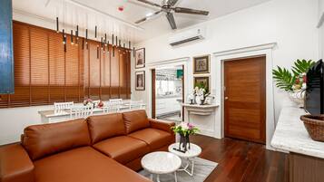 Una sala de estar moderna con un sofá de cuero marrón, dos mesas redondas blancas, un ventilador de techo y persianas de madera.