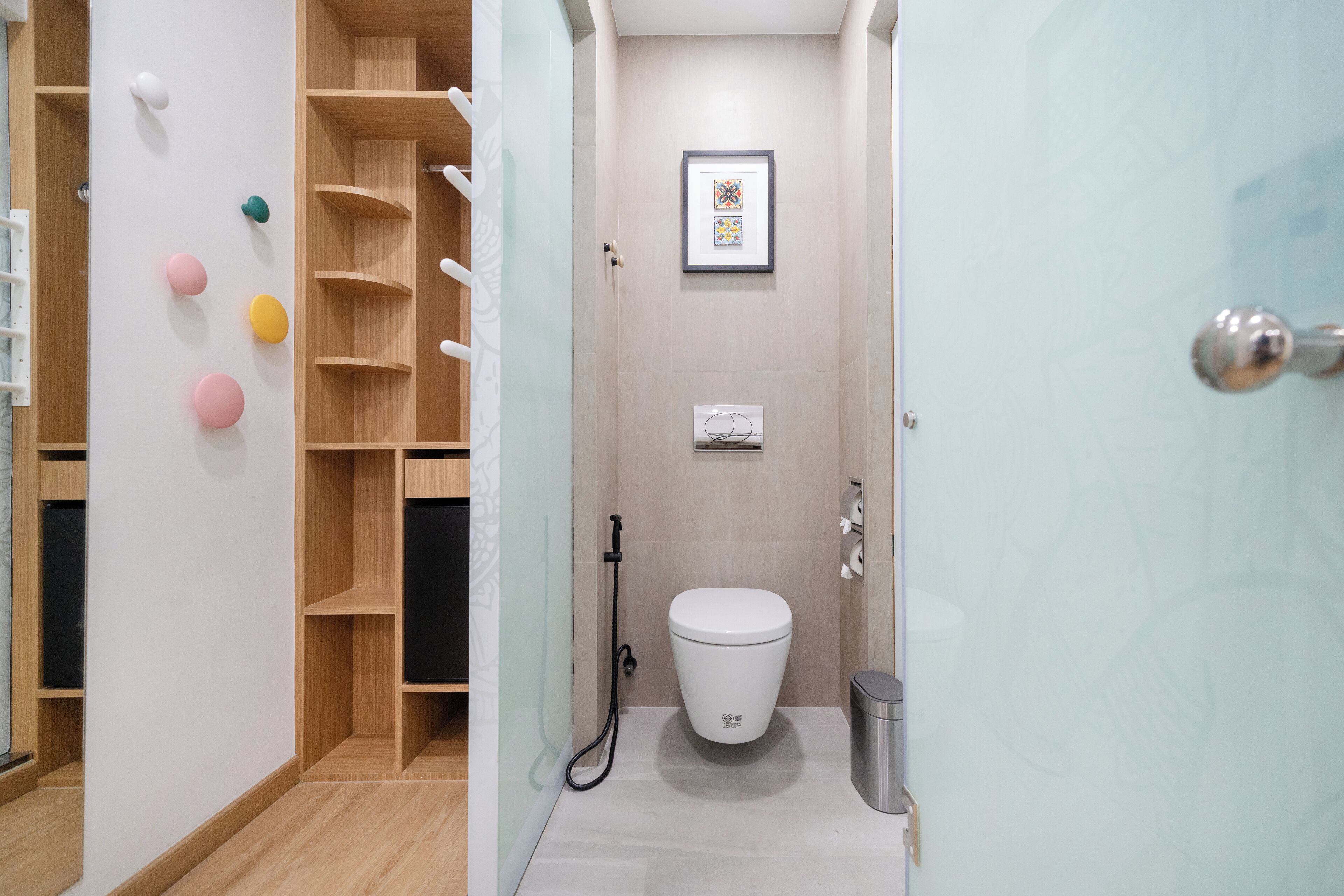 A modern bathroom with a toilet, a shower, and a sink. There are wooden shelves and a framed picture on the wall.