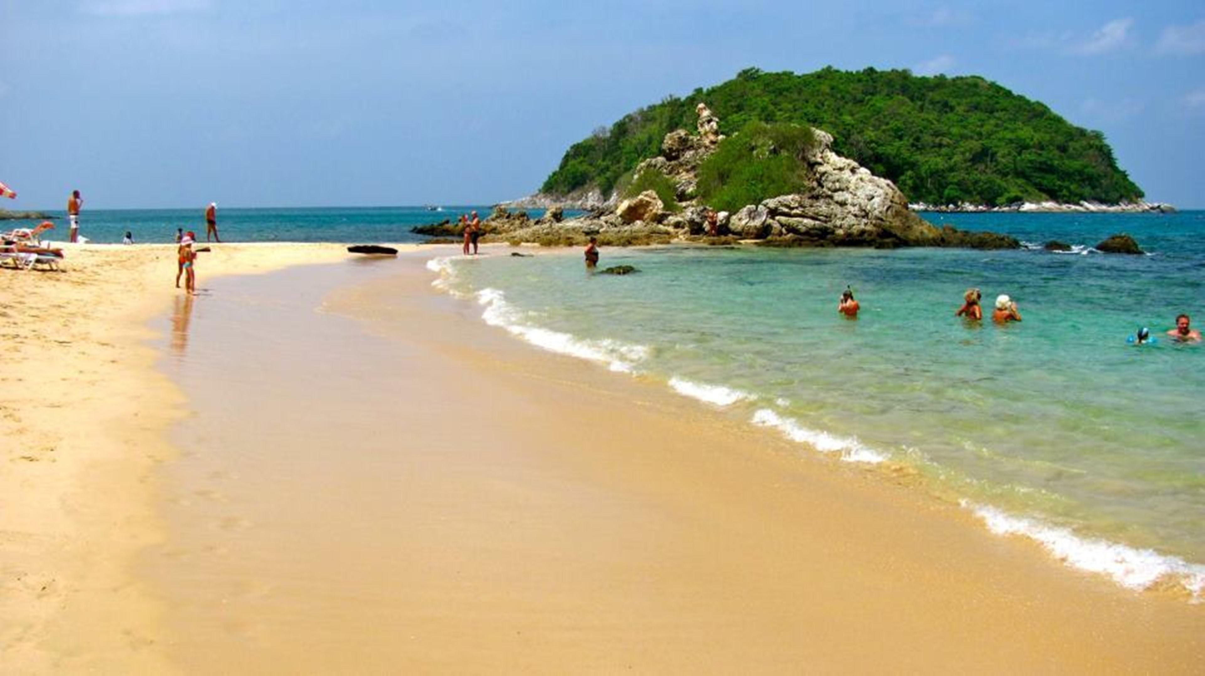 A beach with clear water, a sandy shore, and a small island with greenery.