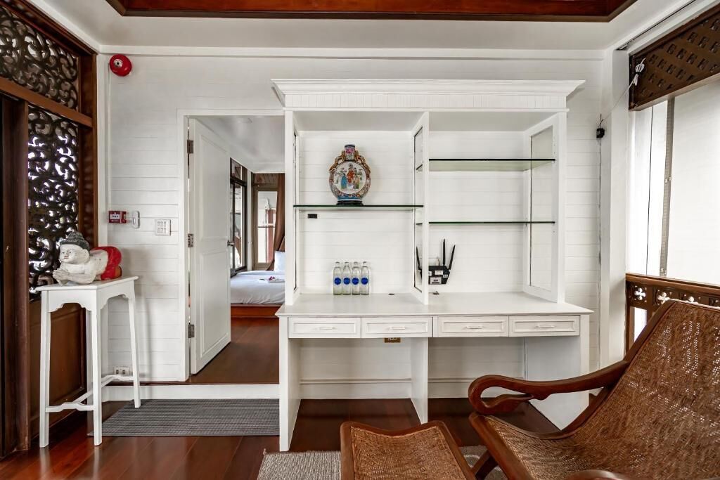 Una habitación con un escritorio blanco, una silla y una estantería con objetos decorativos.