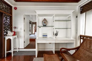 Um quarto com uma escrivaninha branca, uma cadeira e uma estante com objetos decorativos.