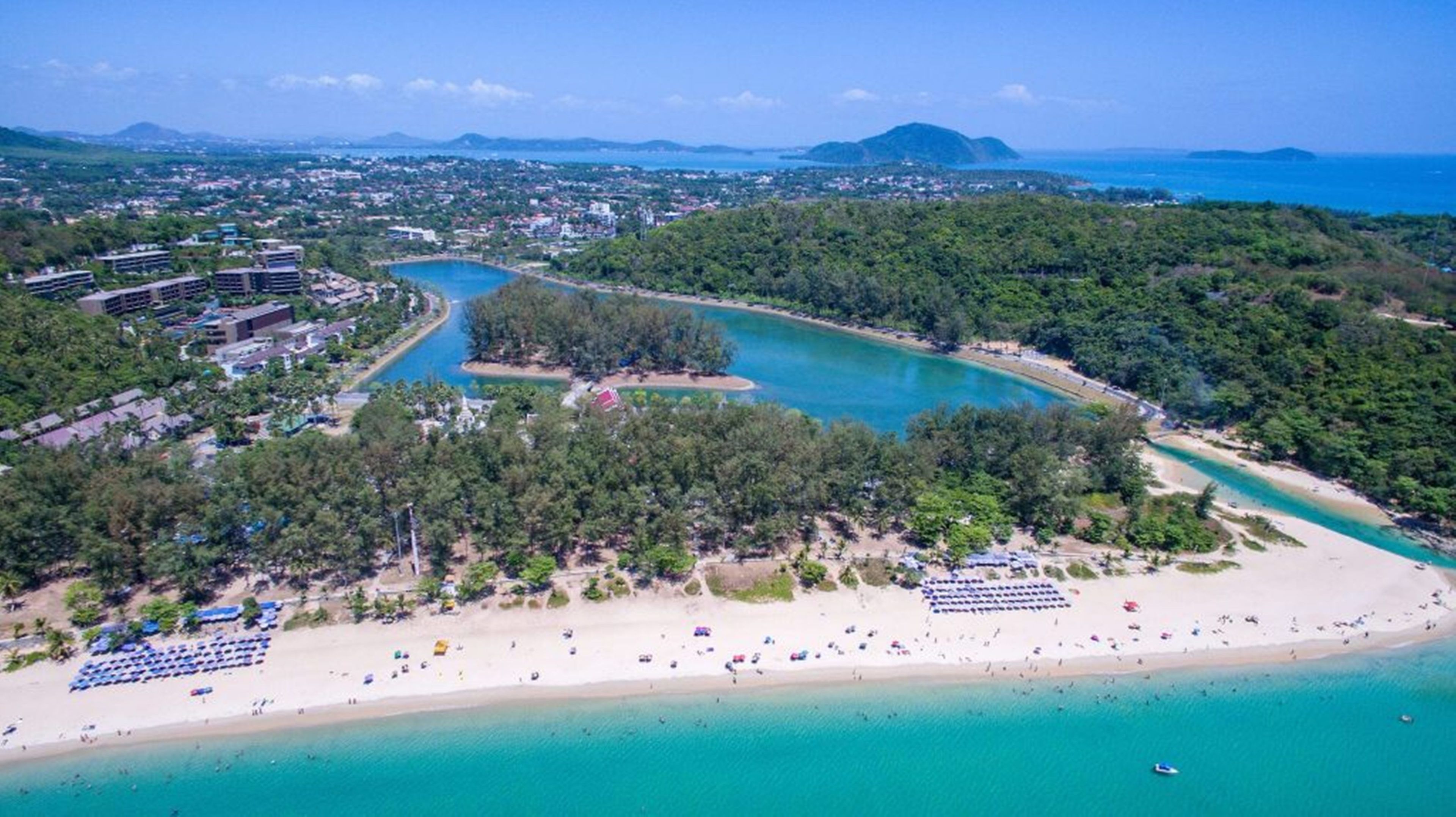 Vista aerea di una zona costiera con spiaggia, un porto turistico e un'area residenziale con edifici.