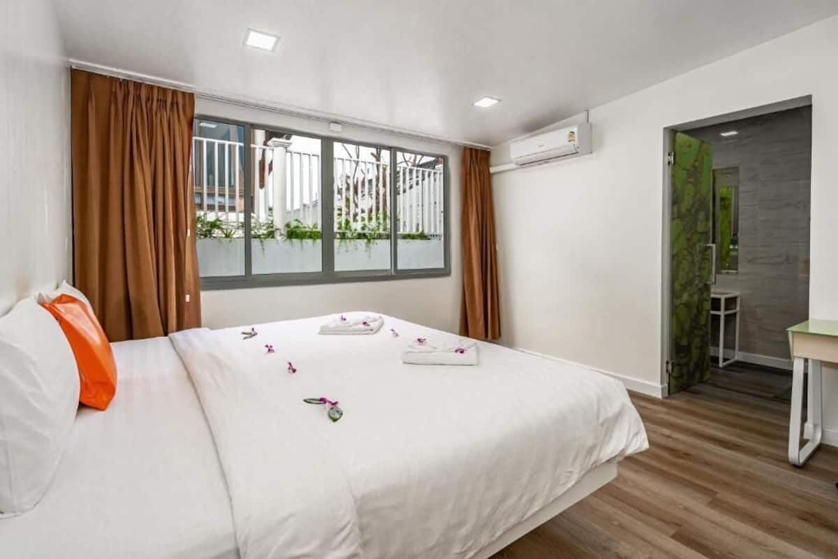Quarto de hotel moderno com uma cama grande, uma escrivaninha e vista para o verde lá fora.