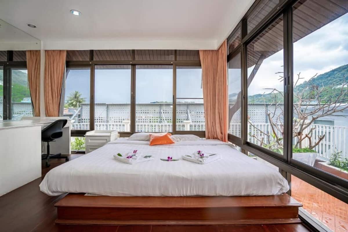 Quarto de hotel moderno com uma cama grande, uma escrivaninha e vista para a água e colinas.