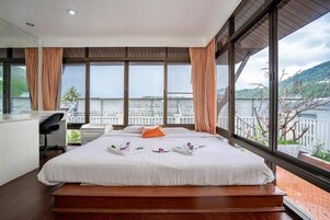 A modern hotel room with a large bed, a desk, and a view of a body of water and hills.