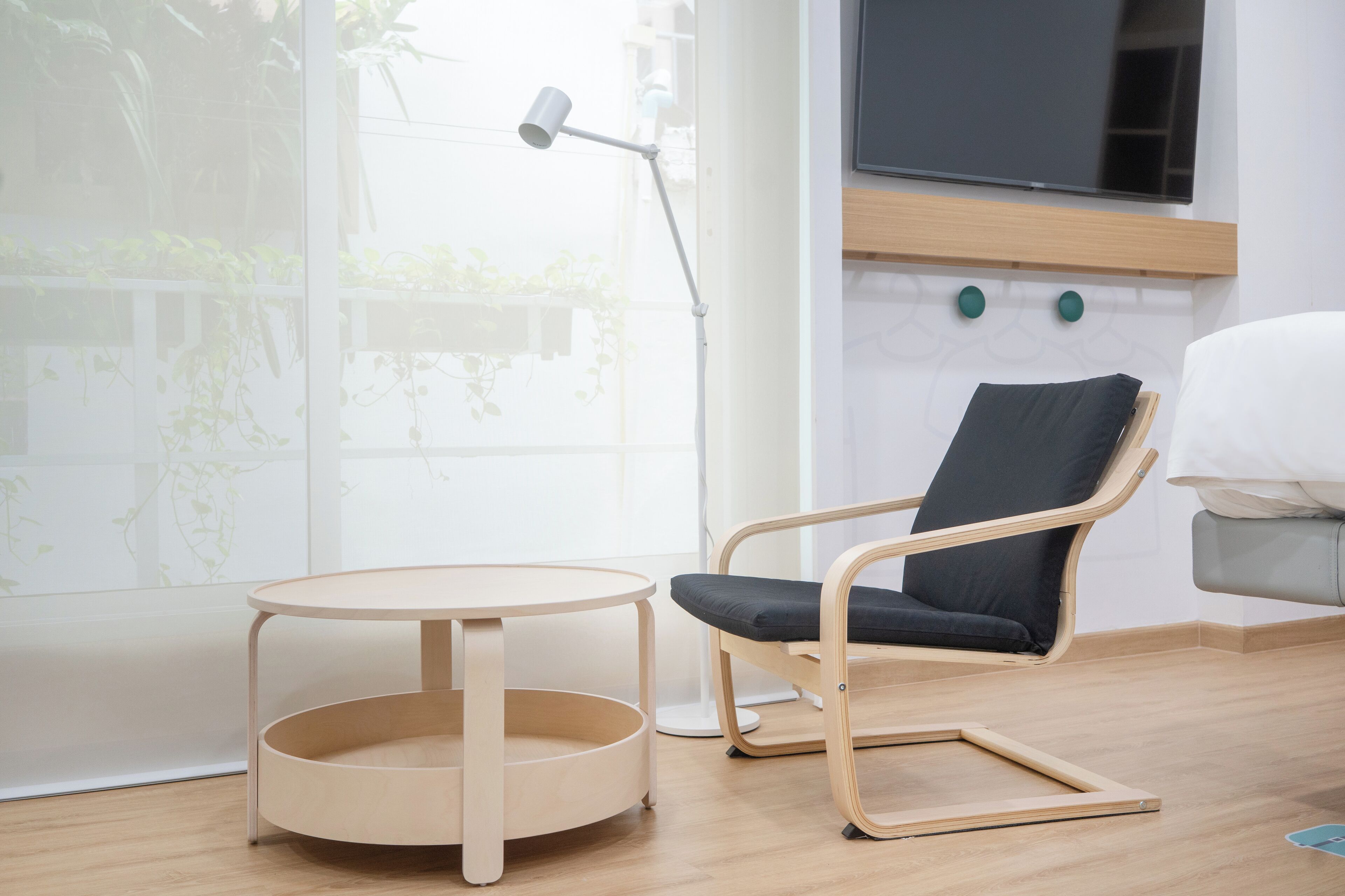 A modern room with a round table, a chair, a TV mounted on the wall, and a window with plants.