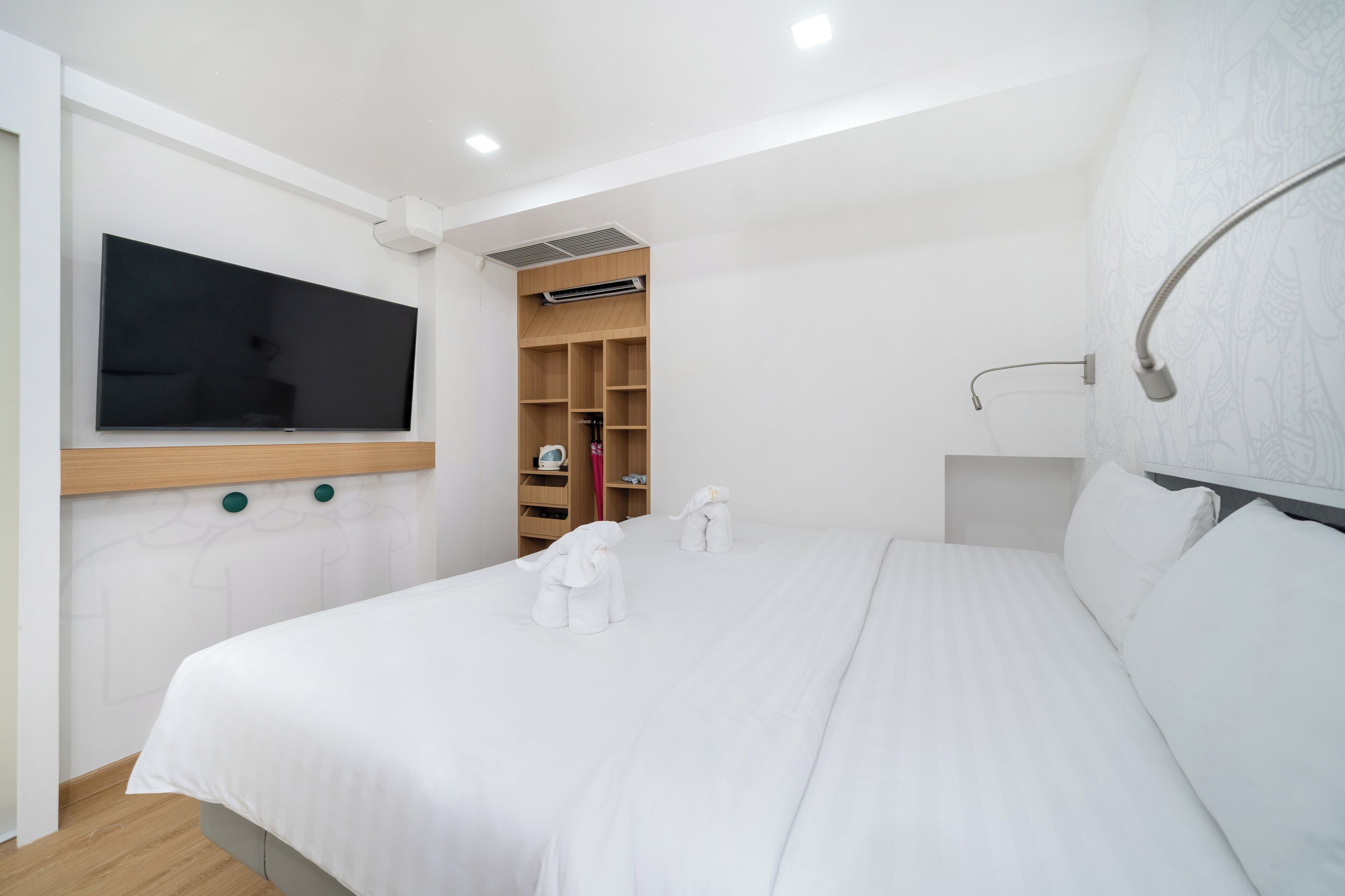 A modern hotel room with a large bed, a flat-screen TV mounted on the wall, a built-in wardrobe, and a shower area.