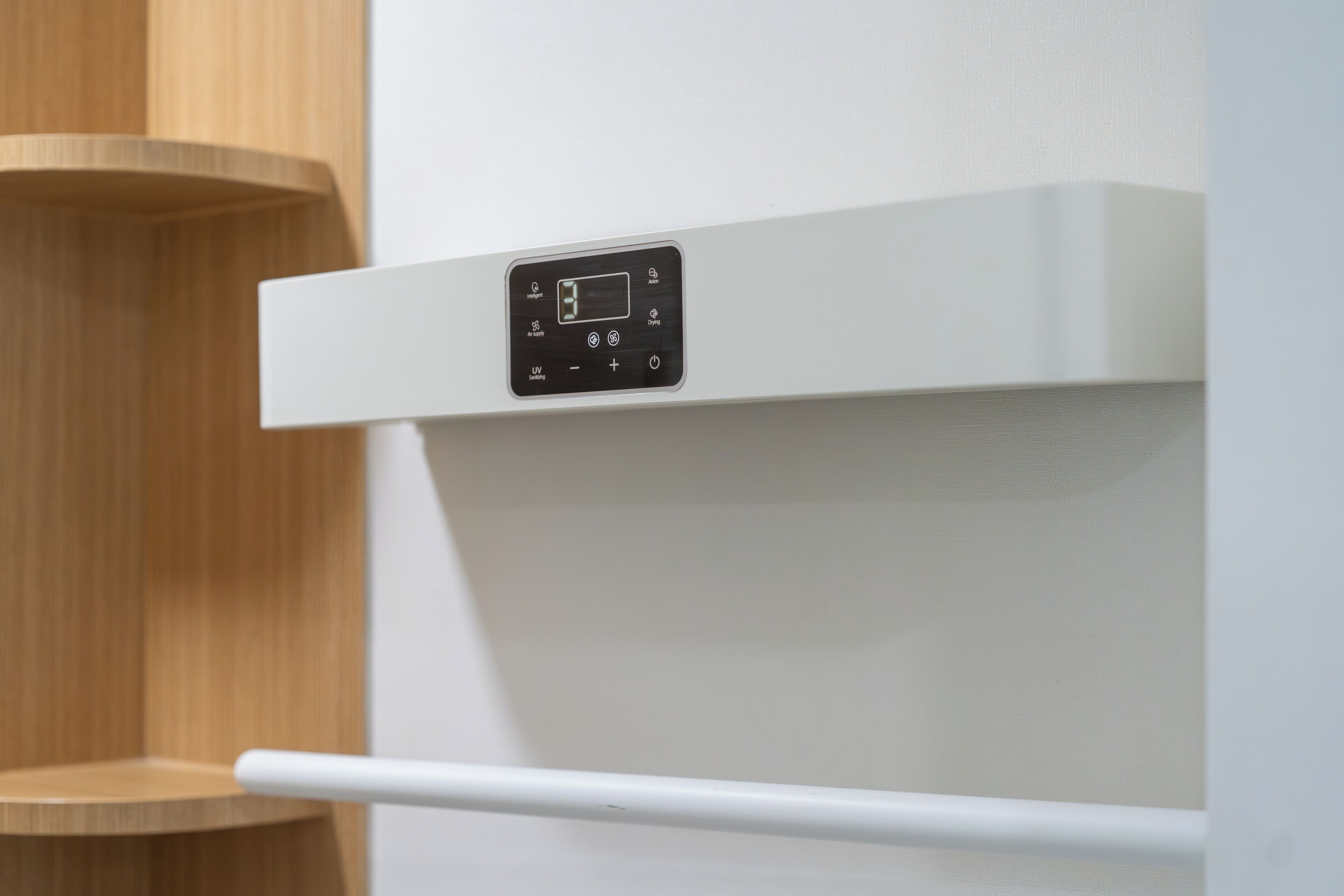 A control panel with a digital display and buttons, mounted on a white wall.
