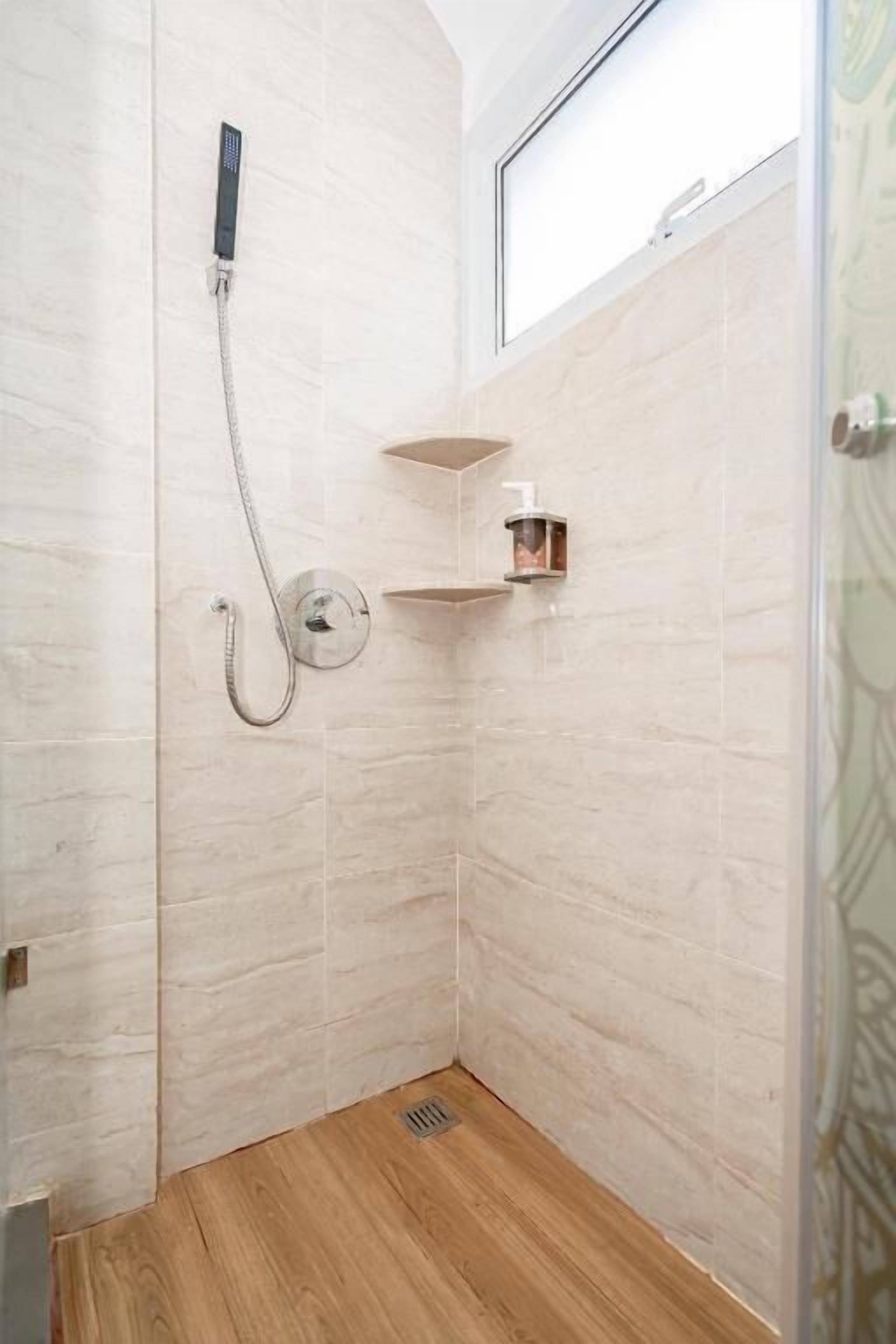 Eine Dusche mit Duschbrause und Wandarmatur, ein kleines Ablagebrett für Toilettenartikel und ein Holzboden.