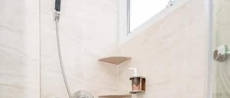 Eine Dusche mit Duschbrause und Wandarmatur, ein kleines Ablagebrett für Toilettenartikel und ein Holzboden.
