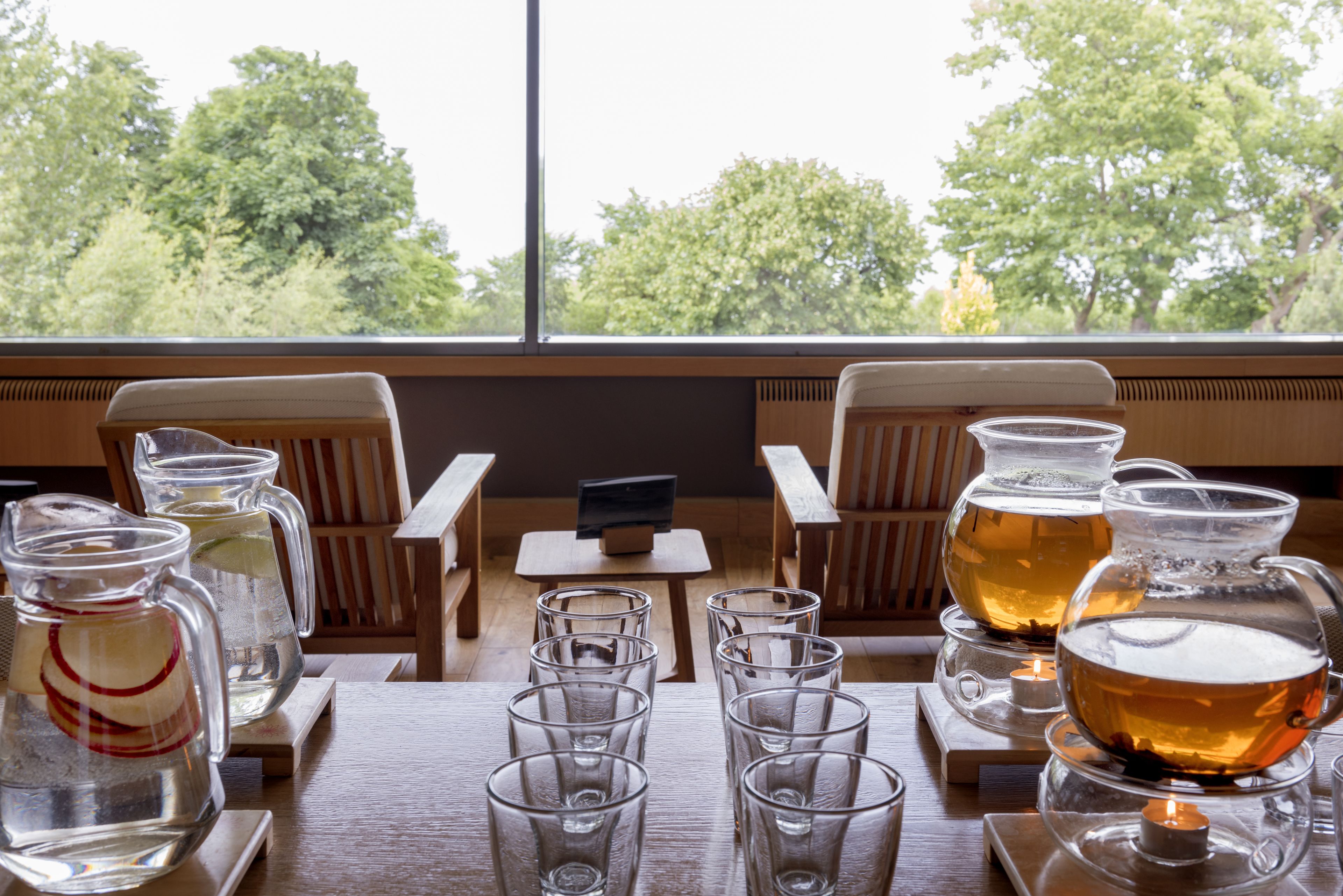 A table set with glasses and a teapot, a small table with a remote control, and a view of trees through a window.