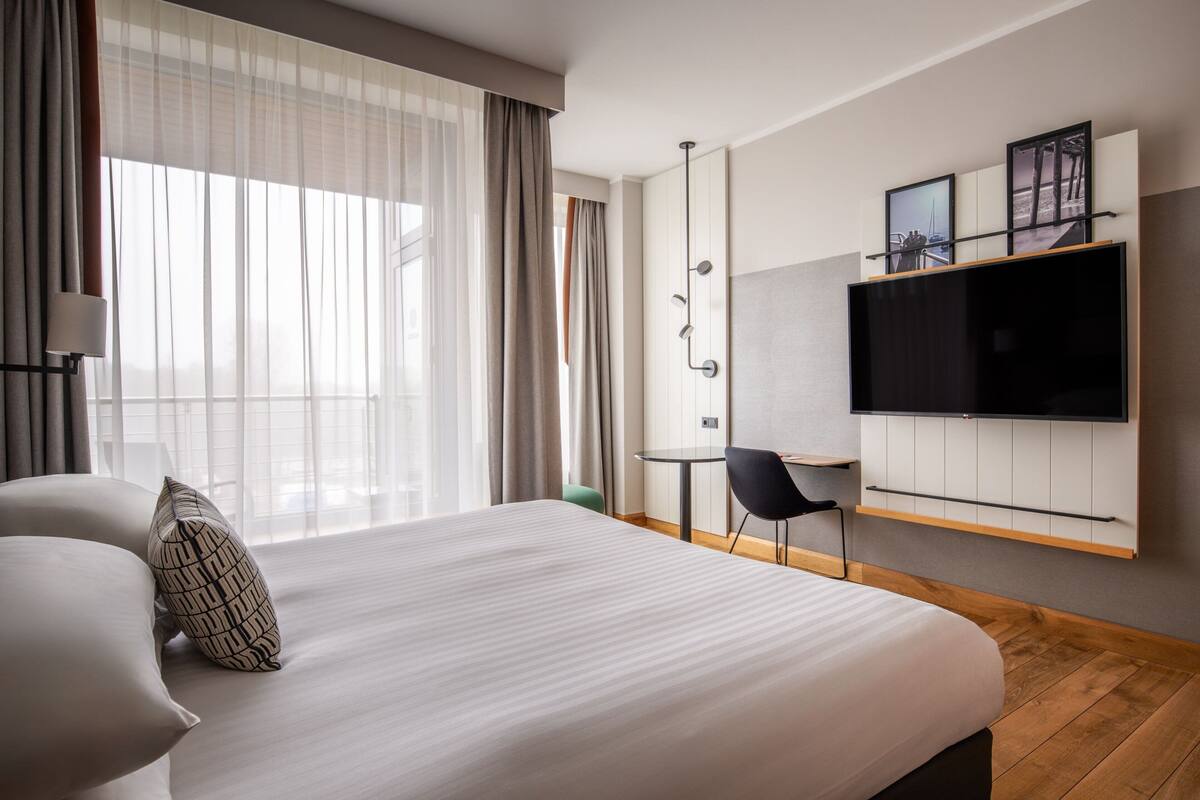Ein modernes Hotelzimmer mit einem großen Bett, einem an der Wand befestigten Fernseher, einem Schreibtisch und einem Stuhl.