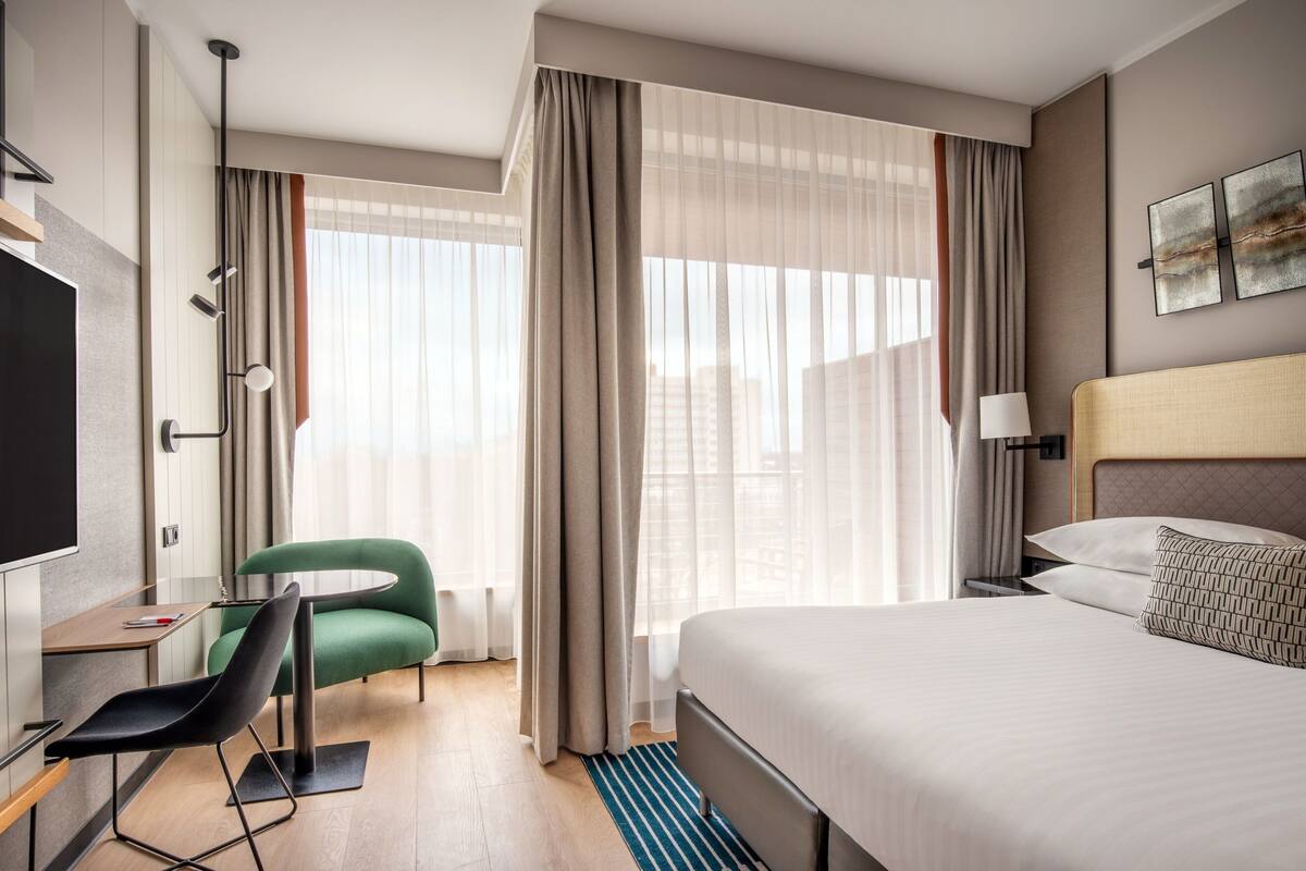 Ein modernes Hotelzimmer mit Bett, Schreibtisch, Stuhl und Fernseher.