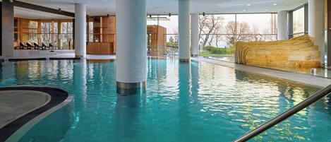 A large indoor swimming pool with clear water, surrounded by modern architecture and large windows.